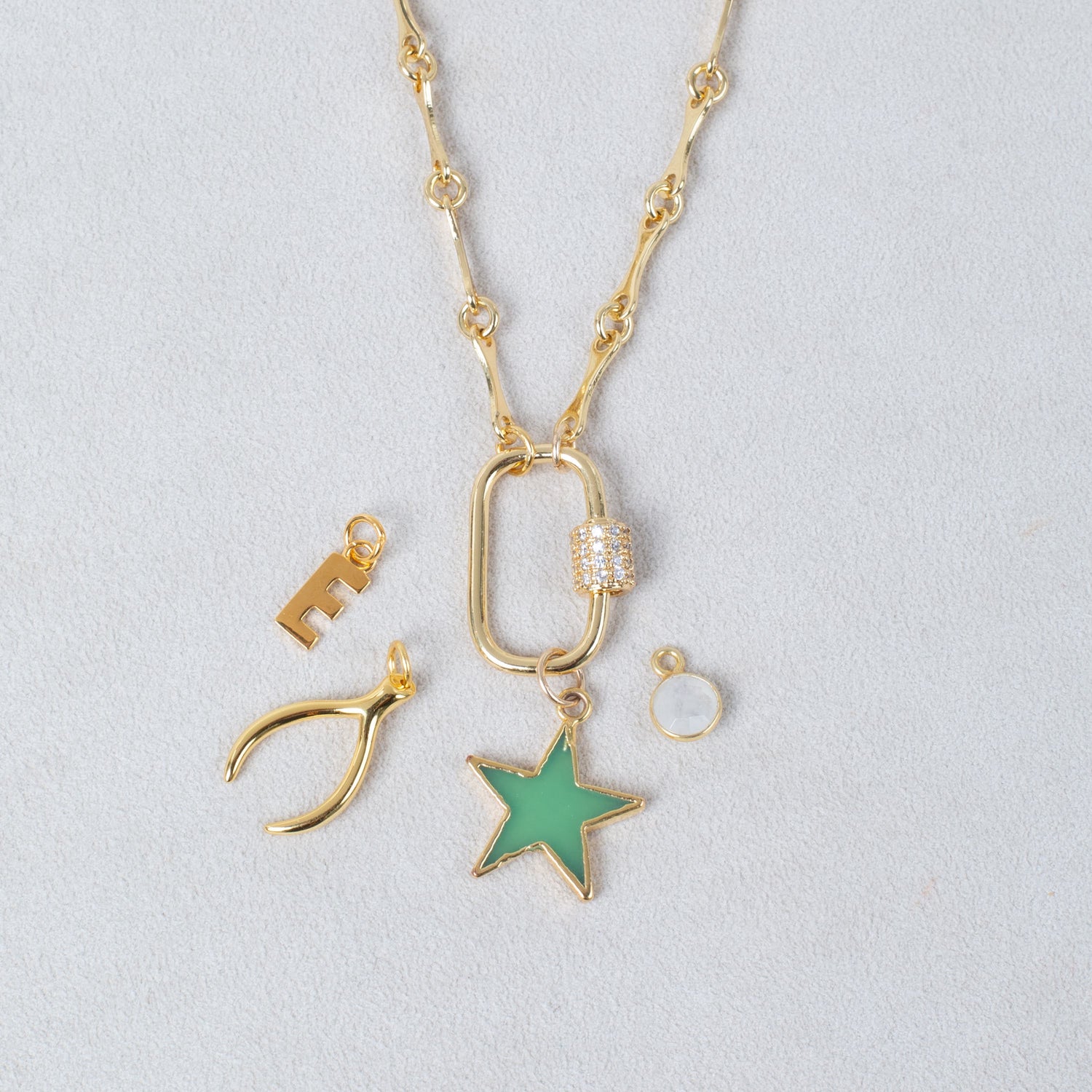 Gold necklace with various pendants including a star, wishbone, and lock on a gray background