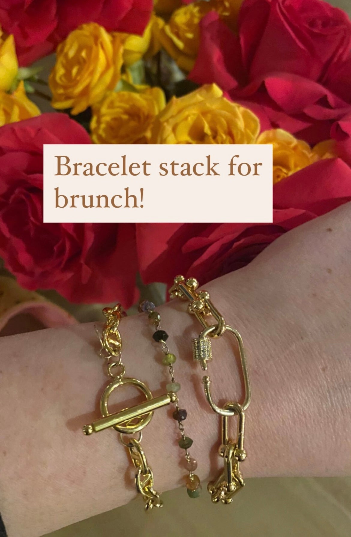 A wrist adorned with two gold bracelets against a backdrop of red and yellow roses